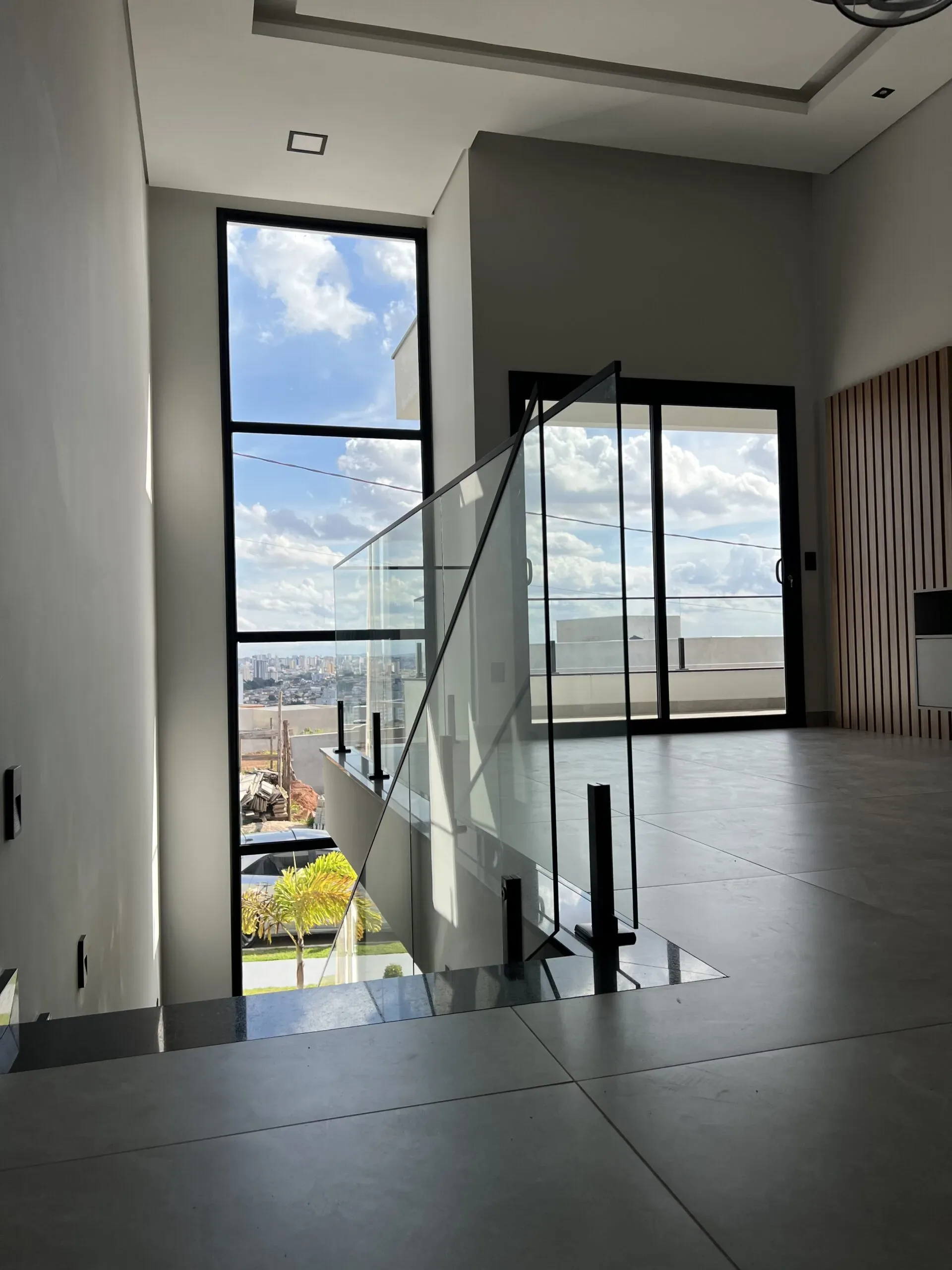 Ambiente interno com janela fixa e porta balcão ao fundo com persiana preta totalmente fechada.