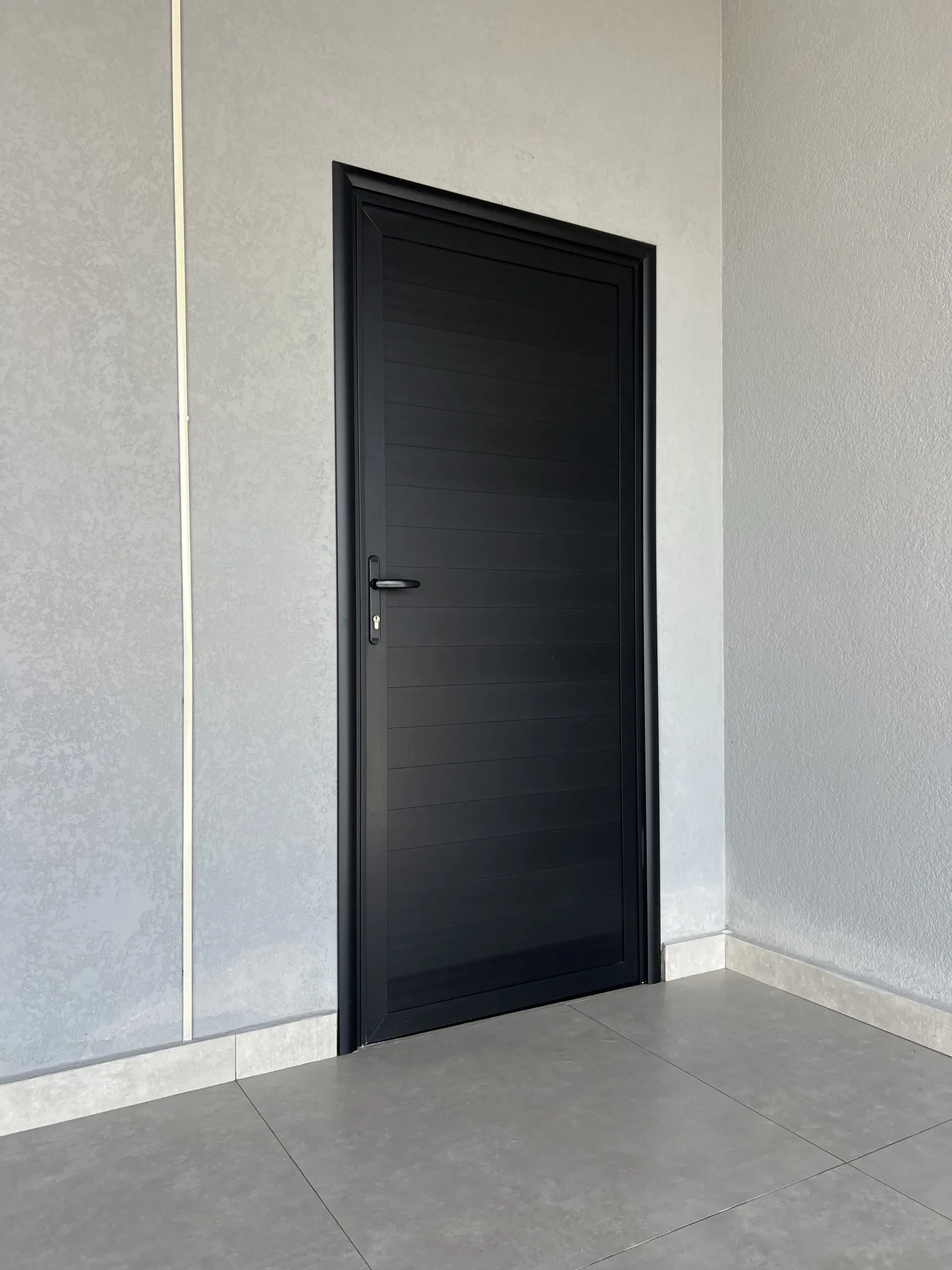 Detalhe de porta de alumínio ripado horizontal em tom escuro, garantindo privacidade e segurança em parede cinza.