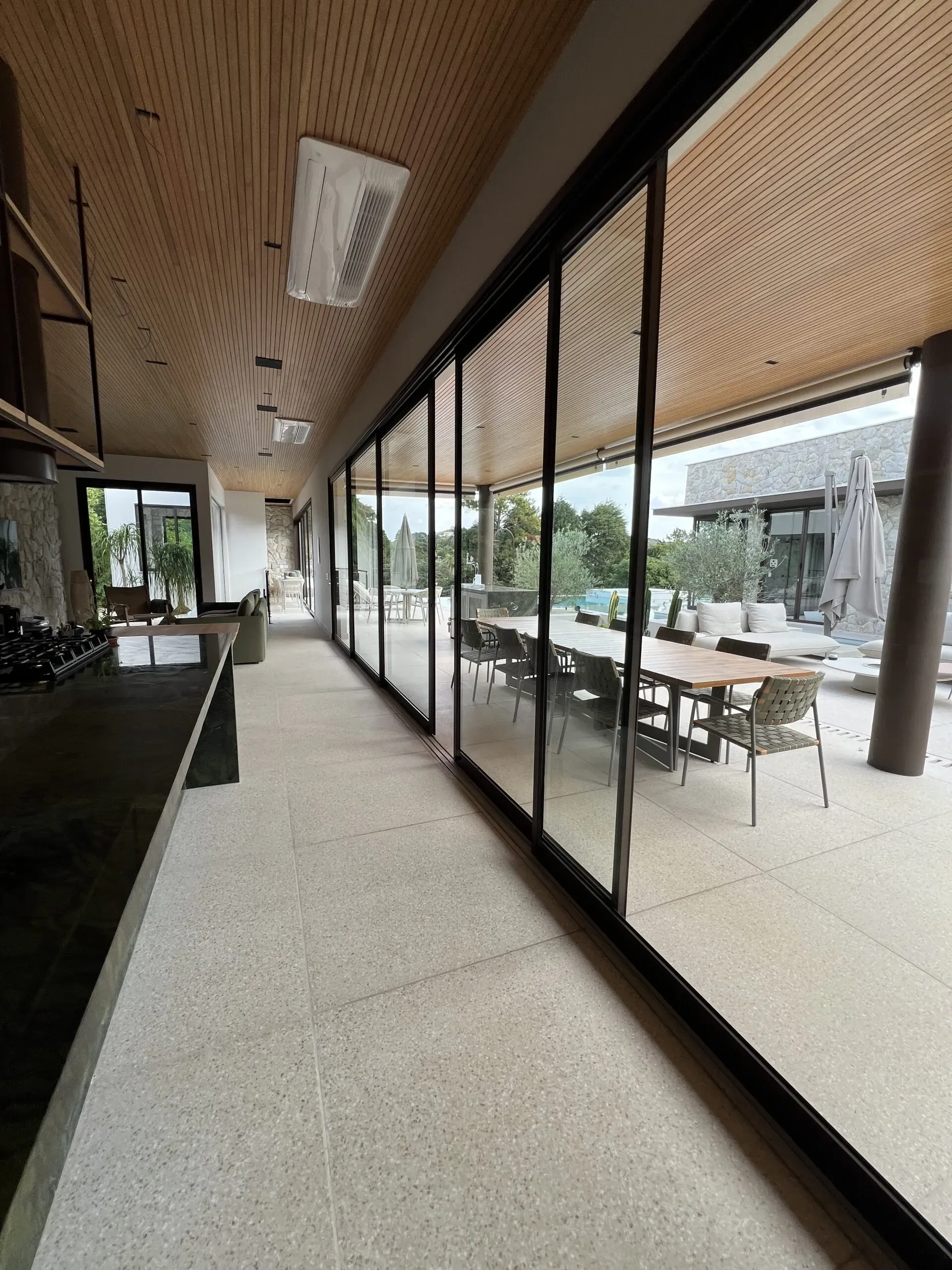 Ampla parede de esquadrias de correr em alumínio preto com vidro temperado integrando sala gourmet à área externa com piscina e jardim.