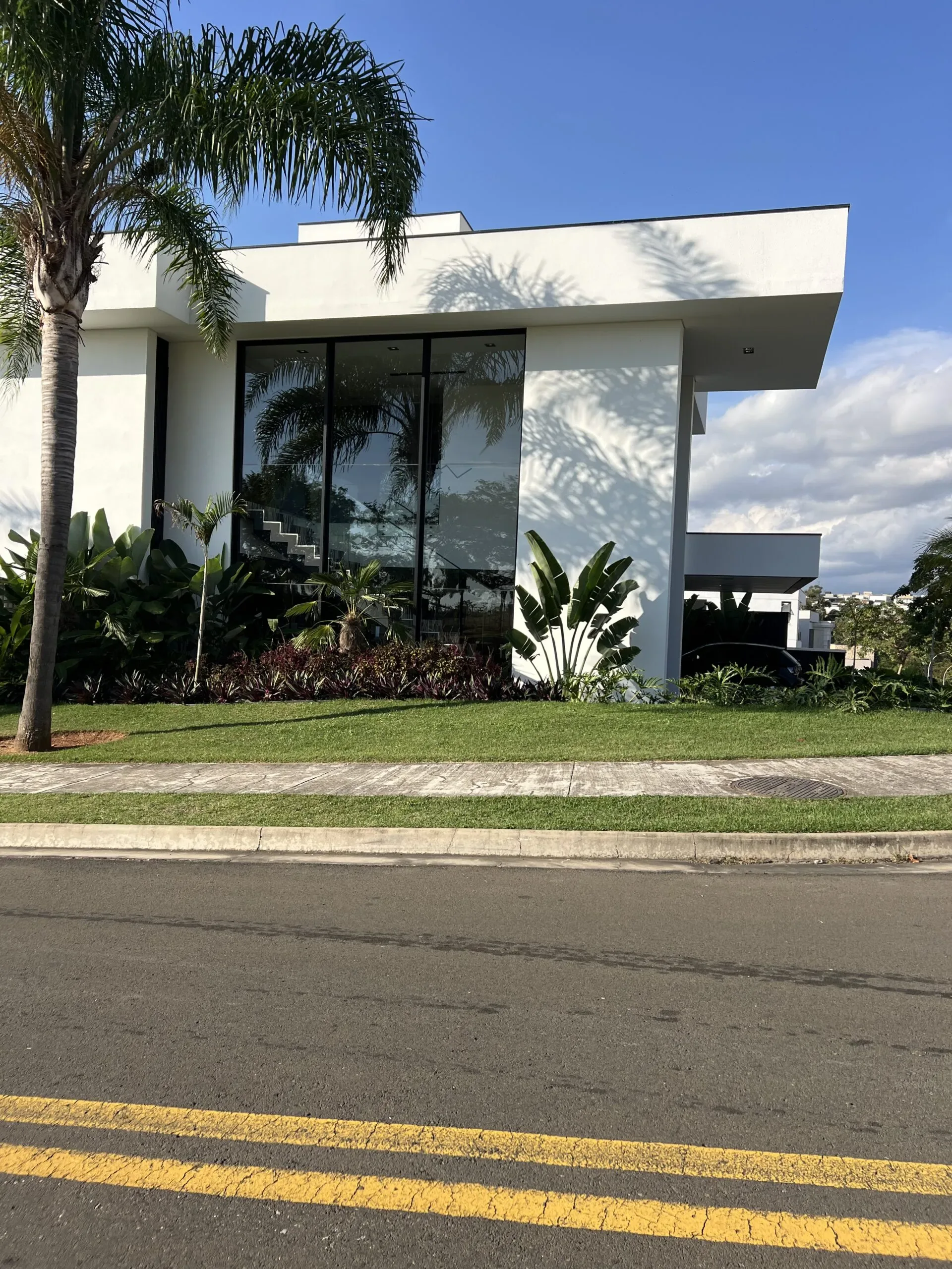 Fachada contemporânea com destaque para guarda-corpo de vidro na varanda superior e amplas janelas com brises.