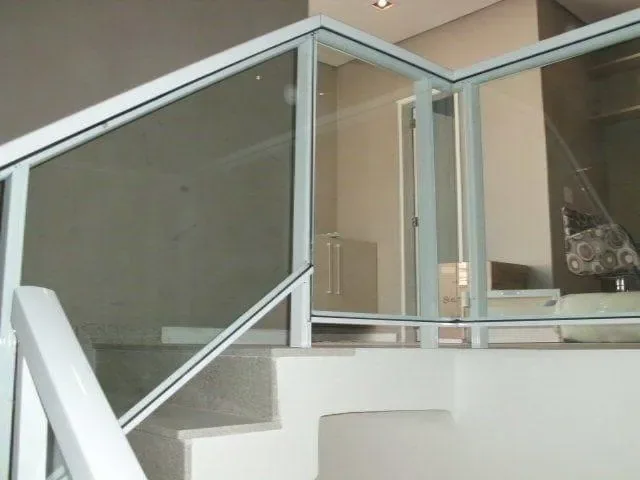 Guarda-corpo em alumínio branco com vidro temperado instalado em escada interna de residência, com degraus em granito e ambiente integrado ao segundo pavimento.
