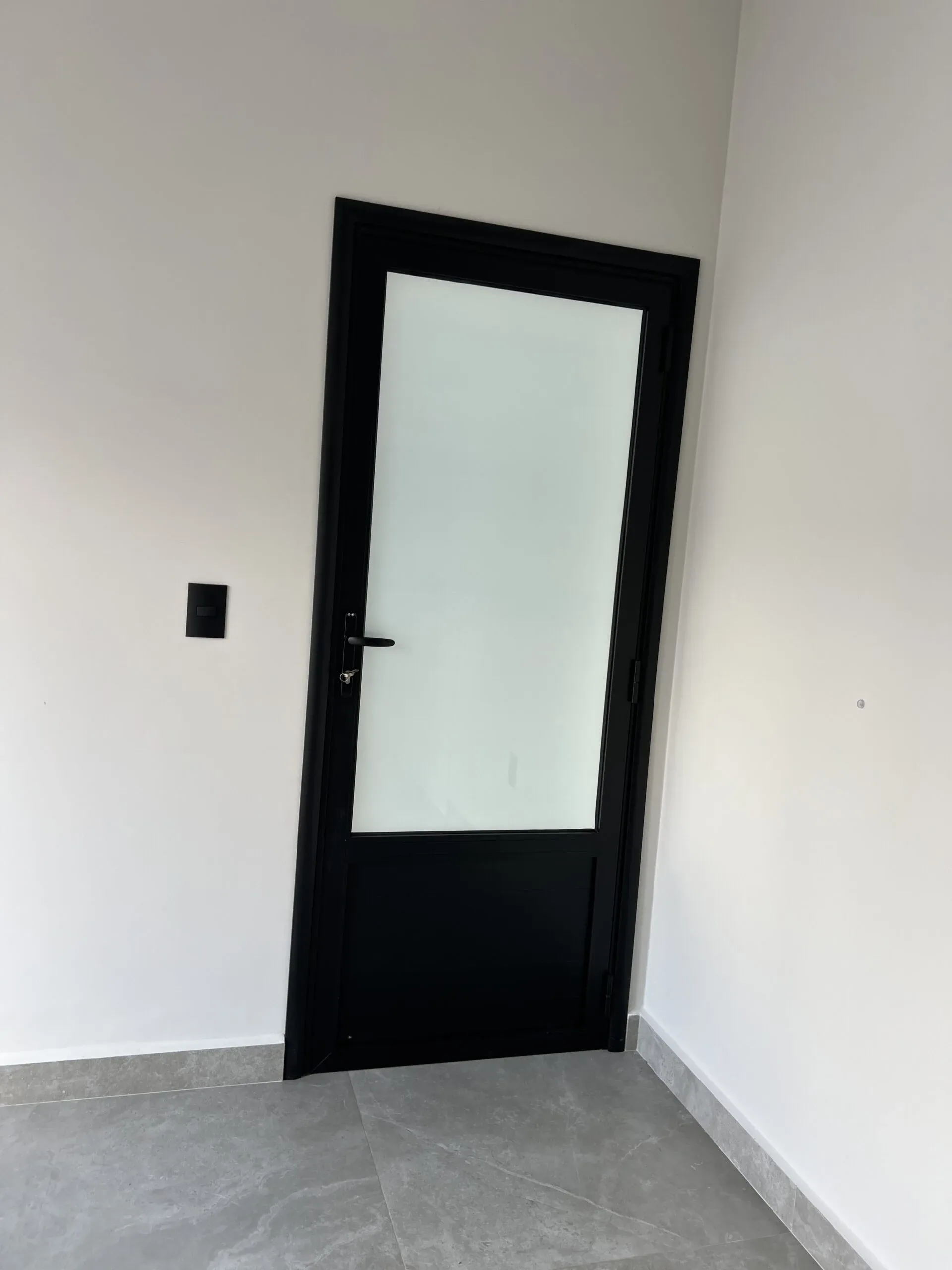 Porta de giro fechada com moldura de alumínio preta e grande painel de vidro leitoso em ambiente claro.