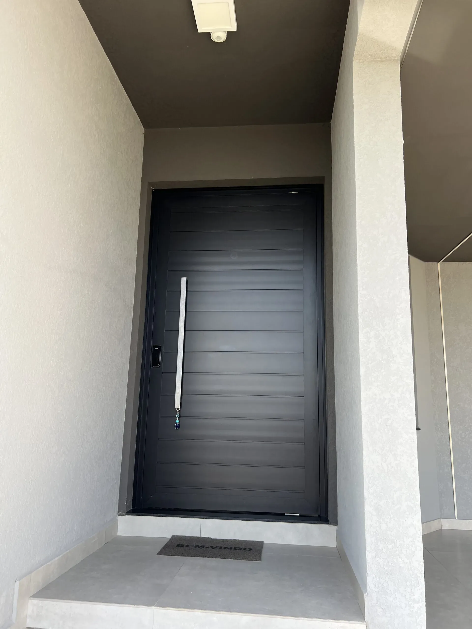 Porta reta e minimalista de tom escuro com linhas horizontais suaves, criando contraste elegante com a parede clara.