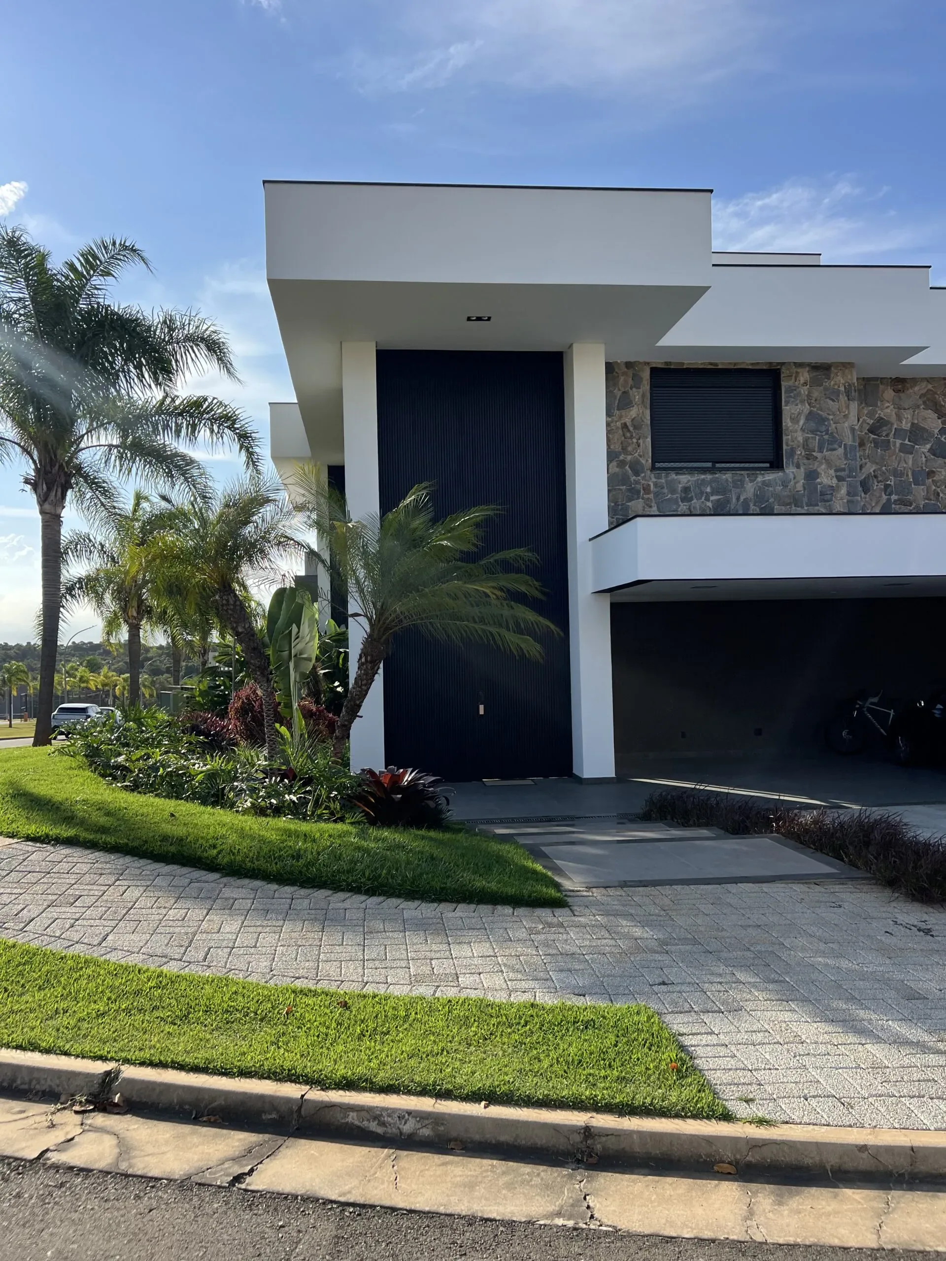 Vista exterior de residência de alto padrão com detalhe para grandes portas de enrolar metálicas marrons integradas à arquitetura.