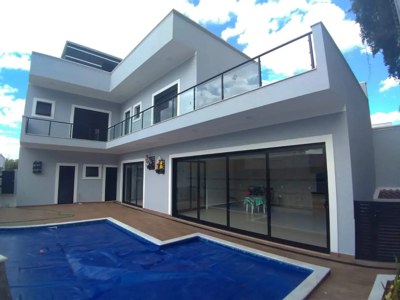 Fachada traseira de casa moderna com esquadrias de correr em alumínio preto, guarda-corpo com tubos pretos no terraço e piscina com deck de madeira em primeiro plano.