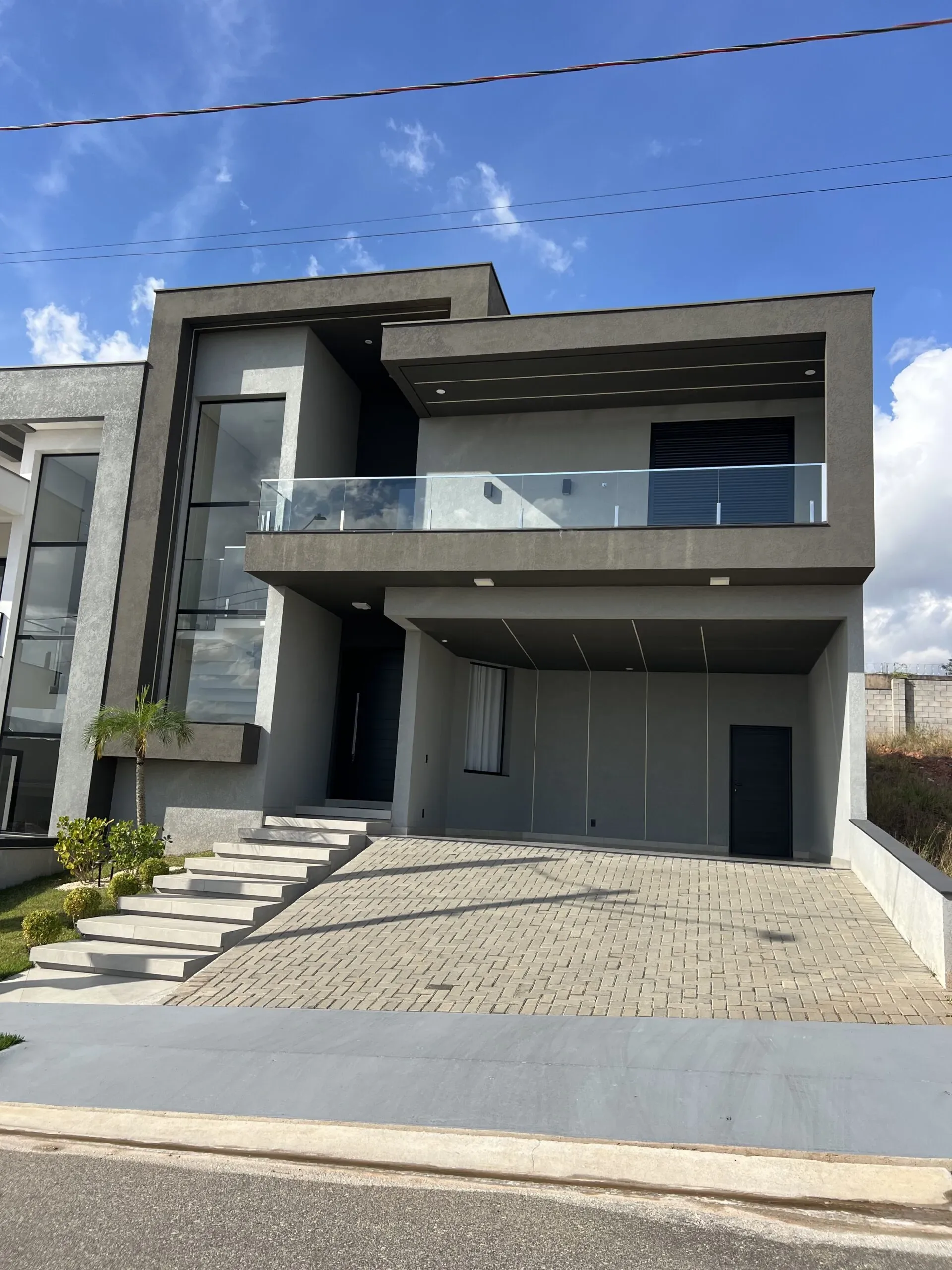 Fachada de residência em tom grafite, com guarda-corpo de vidro e esquadrias escuras.